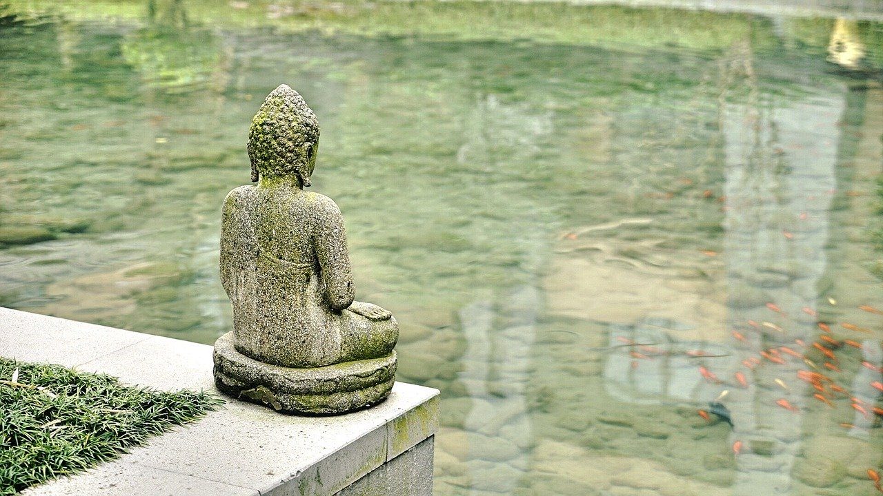 A serene stone Buddha statue beside still green water
