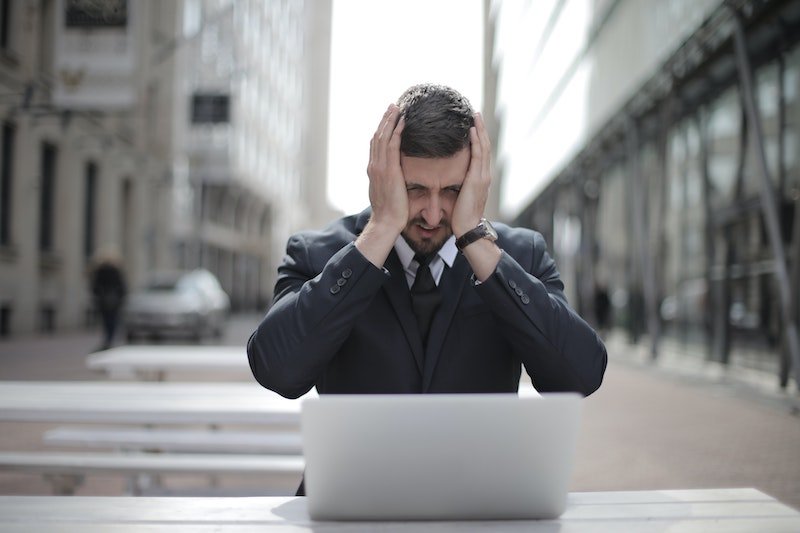 A professional in a suit, head in hands at his laptop